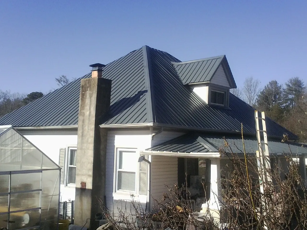 Dark blue standing seam metal roof on a white farmhouse with dormer — Slate & Tile Roof Repair by Roofing Brothers in Harrisonville