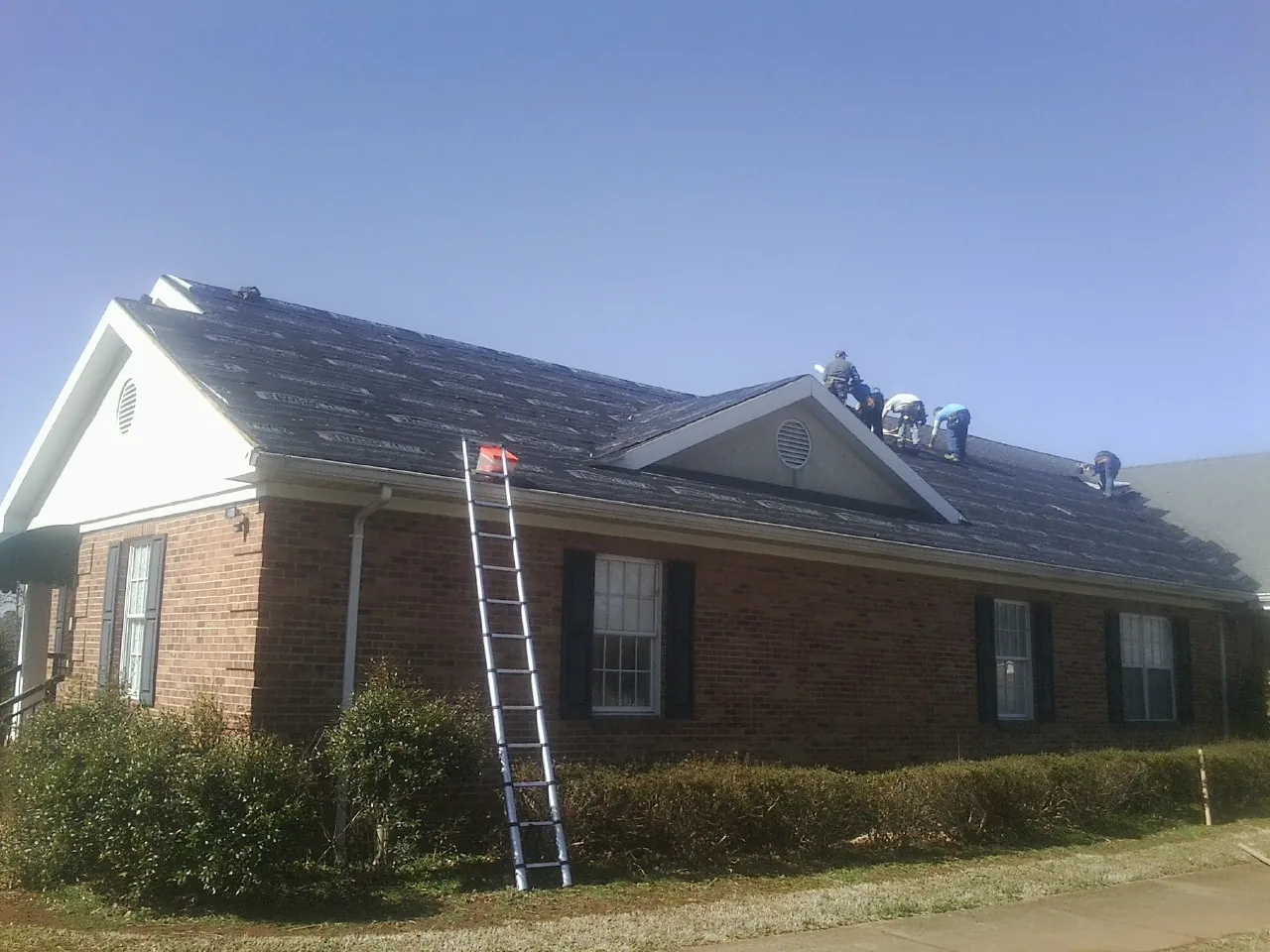 Crew tearing shingles off a brick ranch roof with a ladder set — Metal Roof Repair work by our crew in Harrisonville