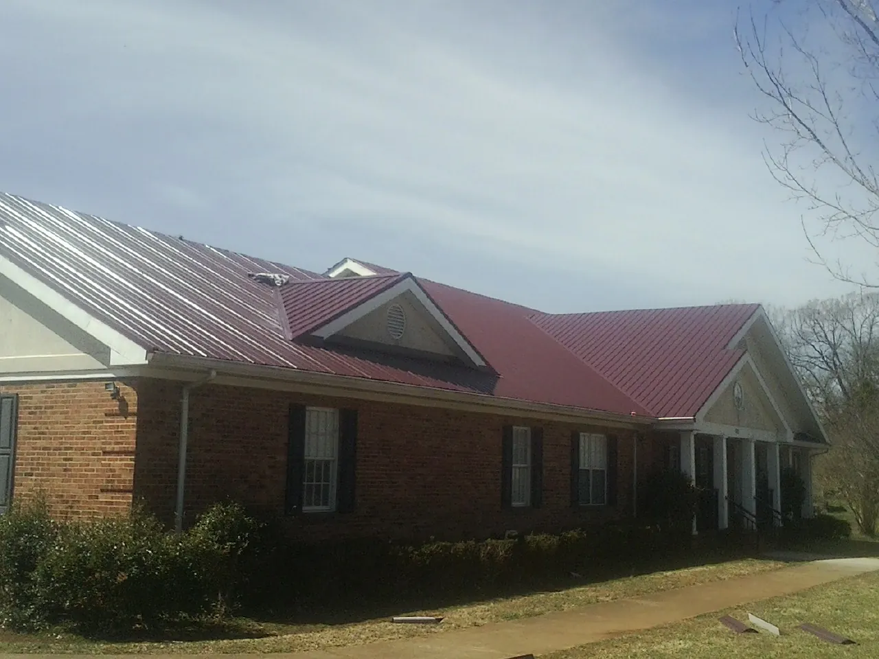 Red metal roof with gabled entries on a long brick building, from a Hail Damage Roof Repair job in Harrisonville