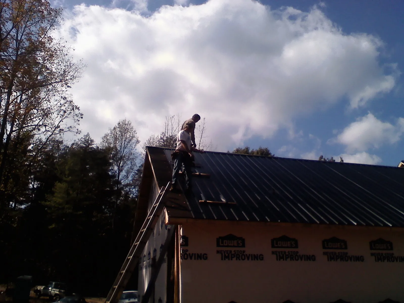 Roofer fastening dark metal panels high against a cloudy sky, from a Roof Inspection job in Harrisonville
