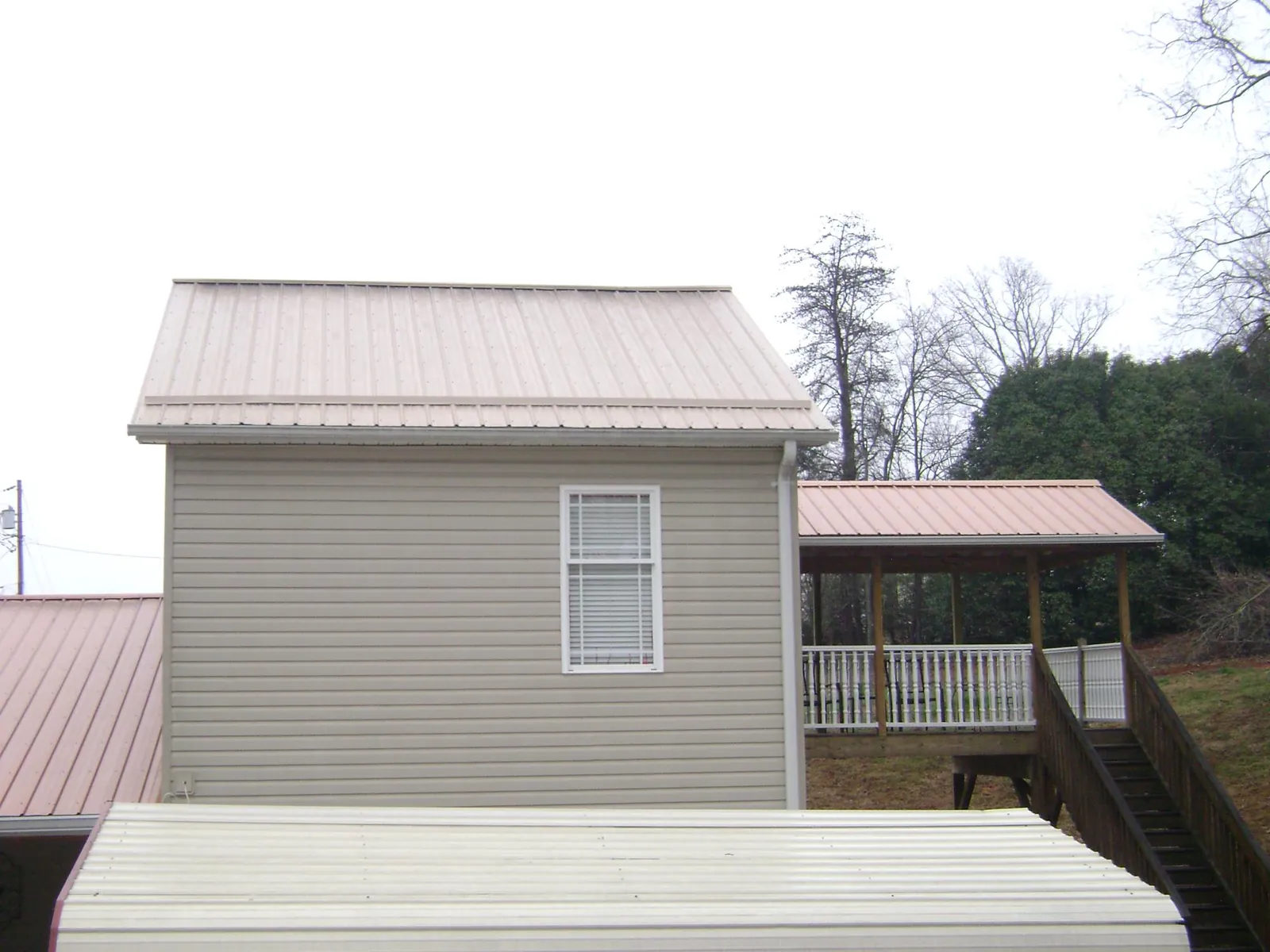 Tan metal roofs on a two story addition and attached porch, from a Roof Replacement job in Harrisonville